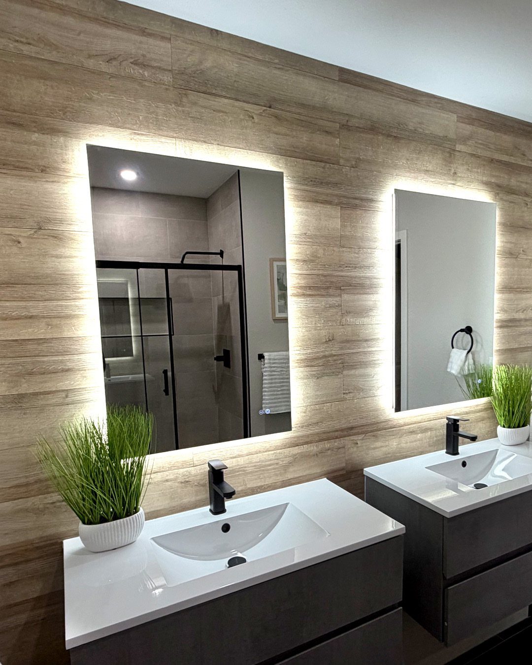 Two white bathroom sinks with black faucets and backlit mirrors against wood-textured wall paneling.