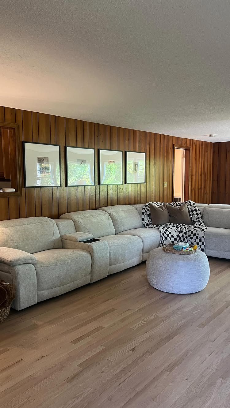 Vertical brown wood paneling on a living room wall behind a grey sectional sofa.