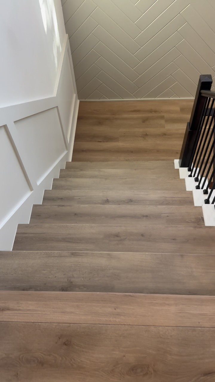 Light LVP Flooring: 5 Design Ideas for Bright Rooms 1 Light oak colored wooden stairs leading down towards a herringbone patterned wall and black railing.