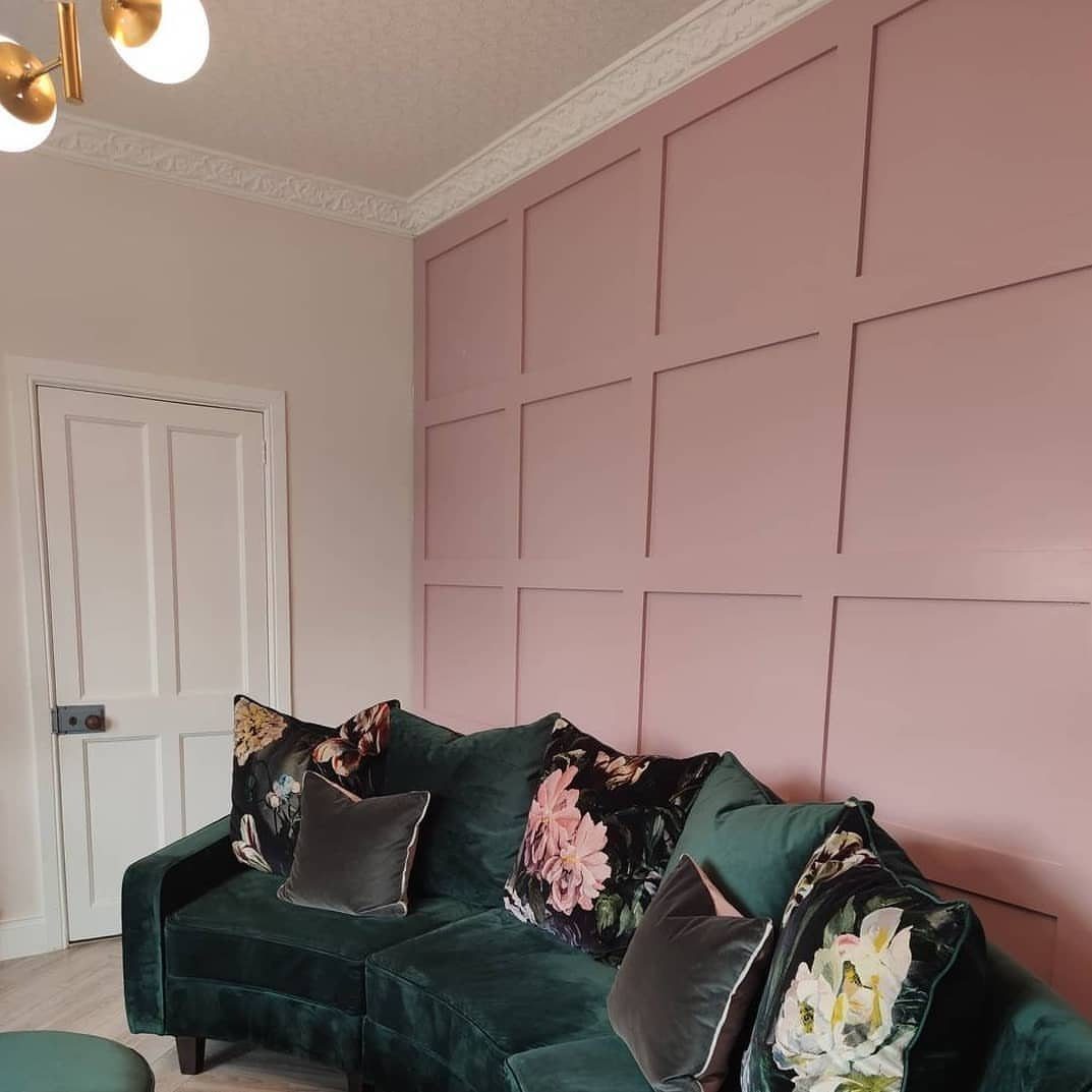 Pink painted wall paneling behind a dark green velvet sofa with floral patterned cushions.