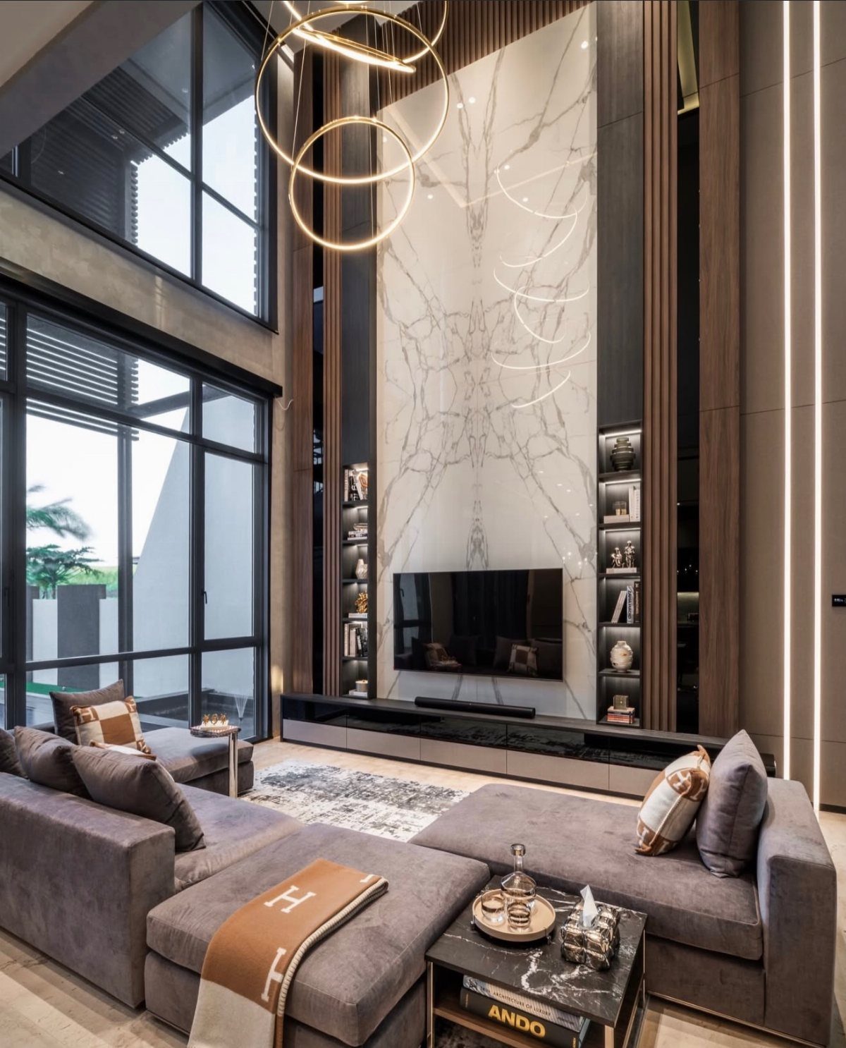 A modern living room with floor-to-ceiling marble and wood paneling surrounding a television.