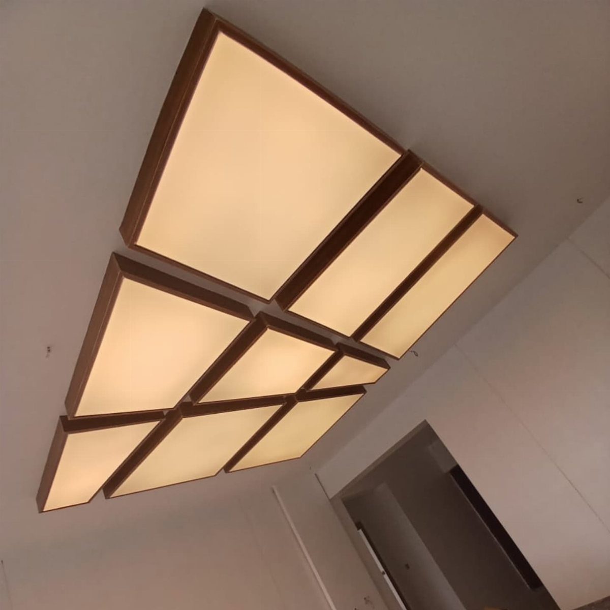 Backlit rectangular ceiling panels with brown wooden frames emitting a warm glow.