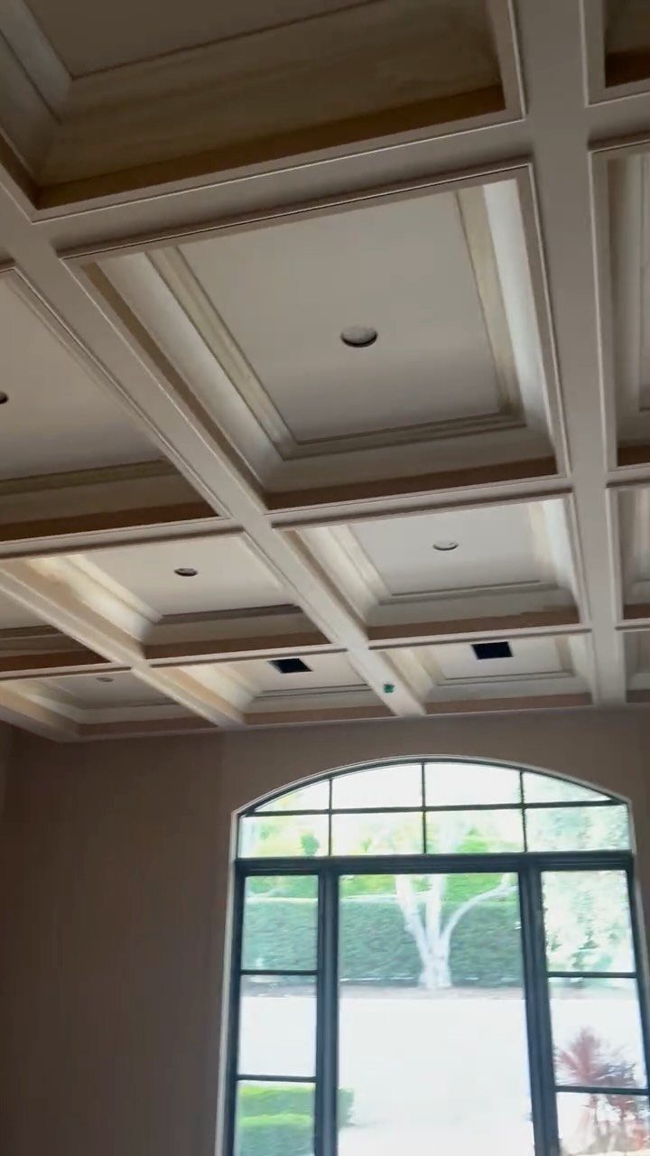 White coffered ceiling with recessed square panels and spotlights above an arched window.