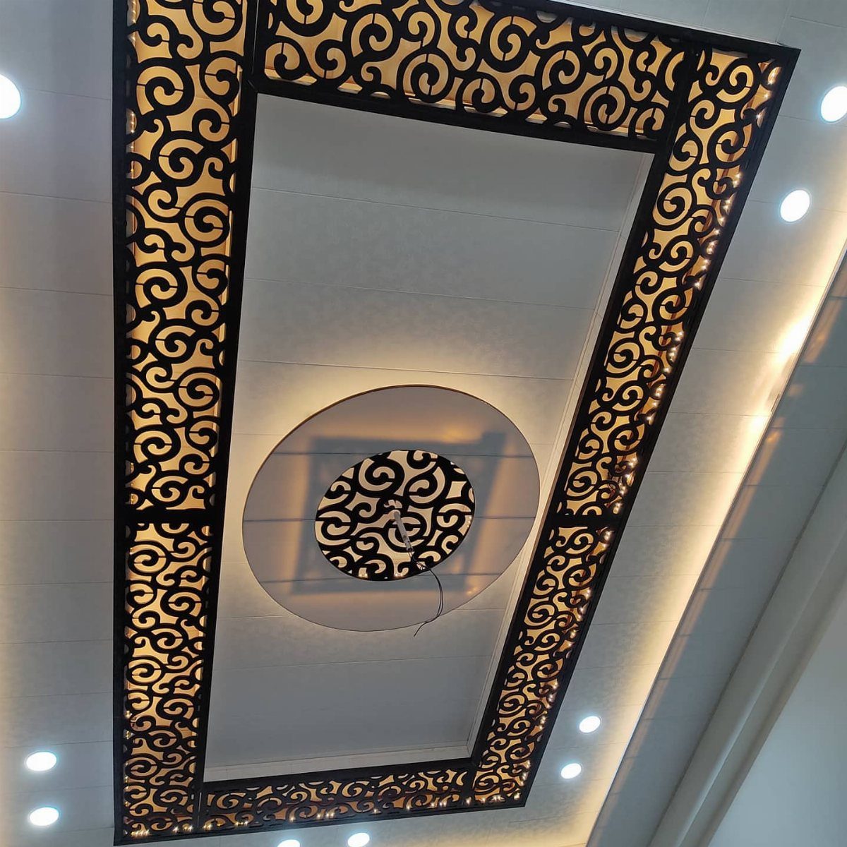 White false ceiling with dark brown intricate jaali patterns in rectangular and circular shapes.