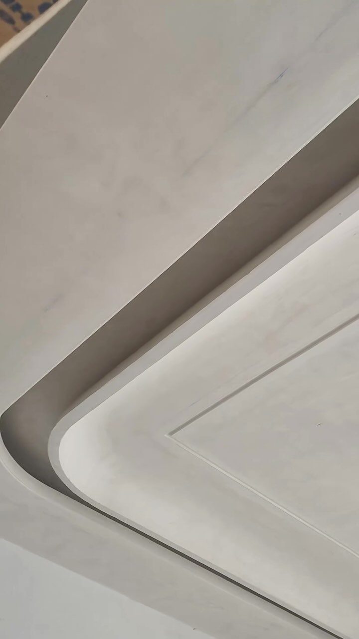 White false ceiling with smooth, layered concentric curves and recessed architectural details.