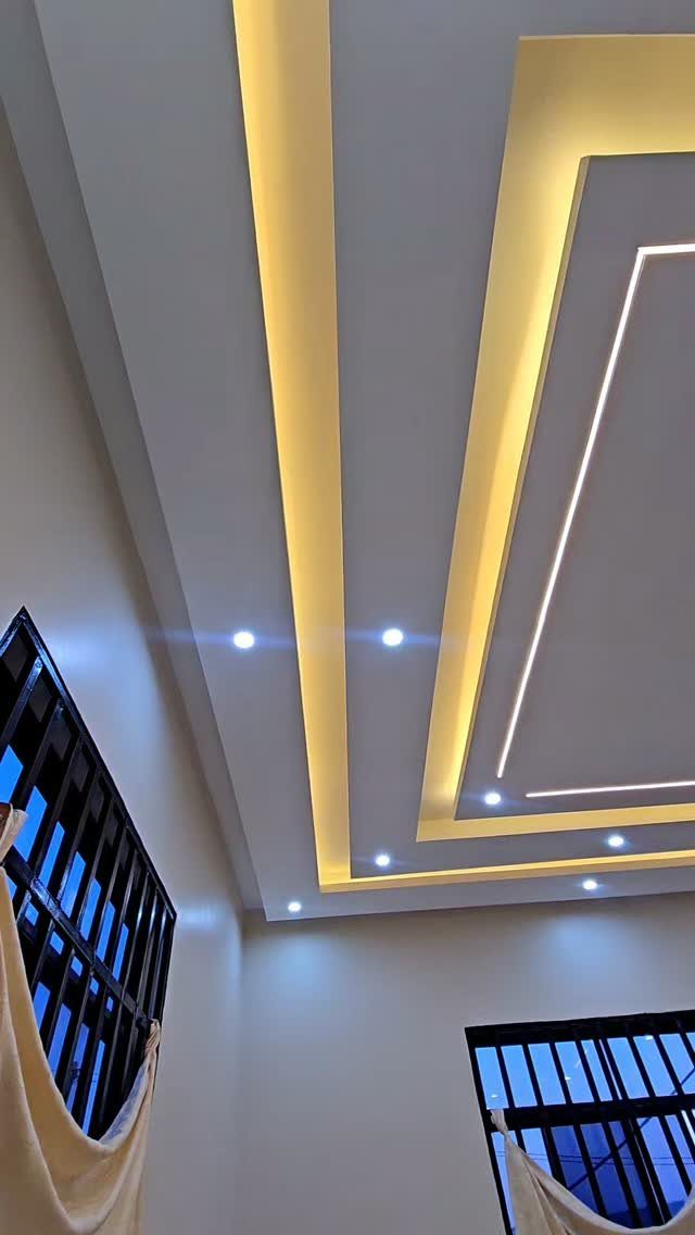 Modern white false ceiling with recessed spotlights and warm yellow cove lighting.