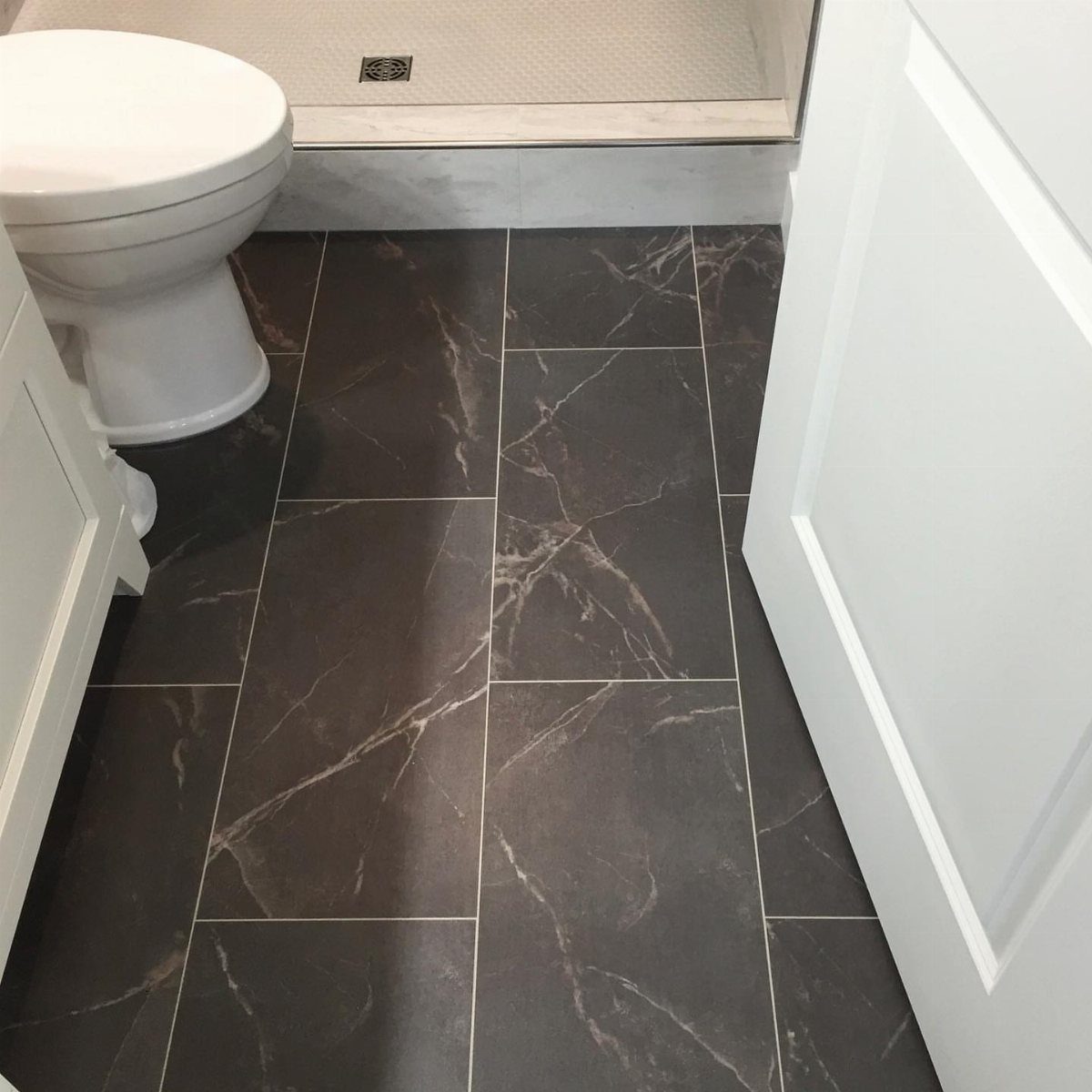 Dark grey marble-effect tiles on a bathroom floor next to a white toilet.