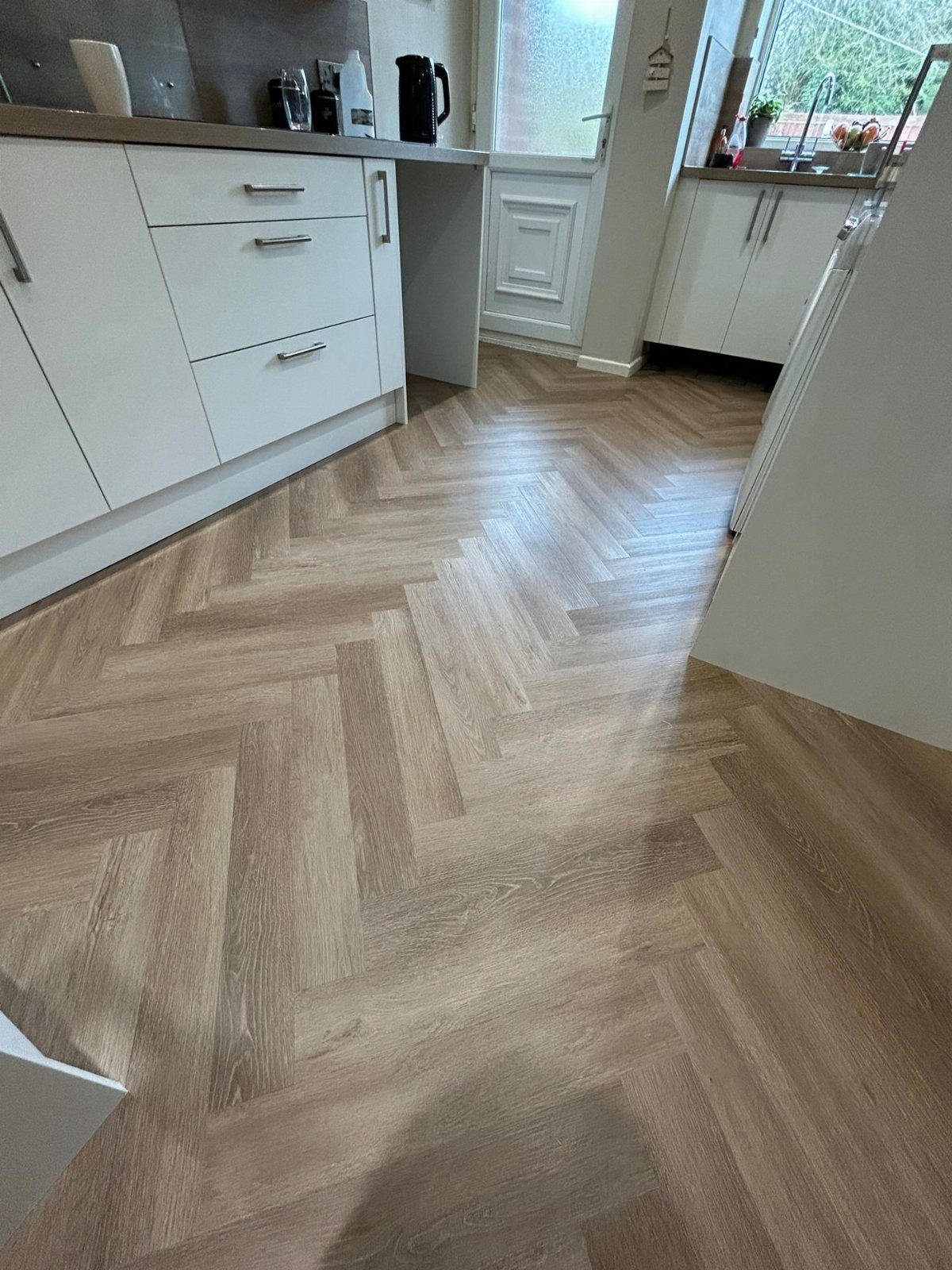 LVP That Looks Like Real Wood: 6 Ideas to Pull It Off 3 Herringbone patterned wood-look flooring installed in a modern white kitchen setting.