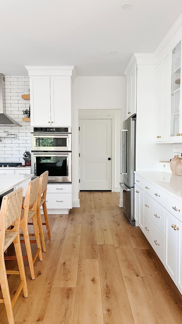 LVP That Looks Like Real Wood: 6 Ideas to Pull It Off 4 Light wood-toned luxury vinyl plank flooring installed in a bright, modern white kitchen.