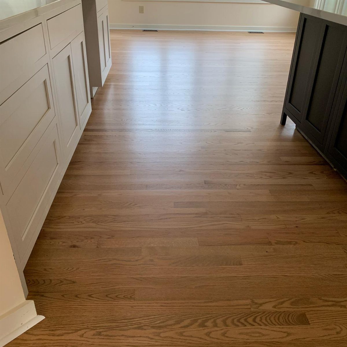 Medium Hardwood Floors: 5 Rooms That Get the Tone Right 5 Light brown hardwood flooring planks installed between white and dark kitchen cabinets.