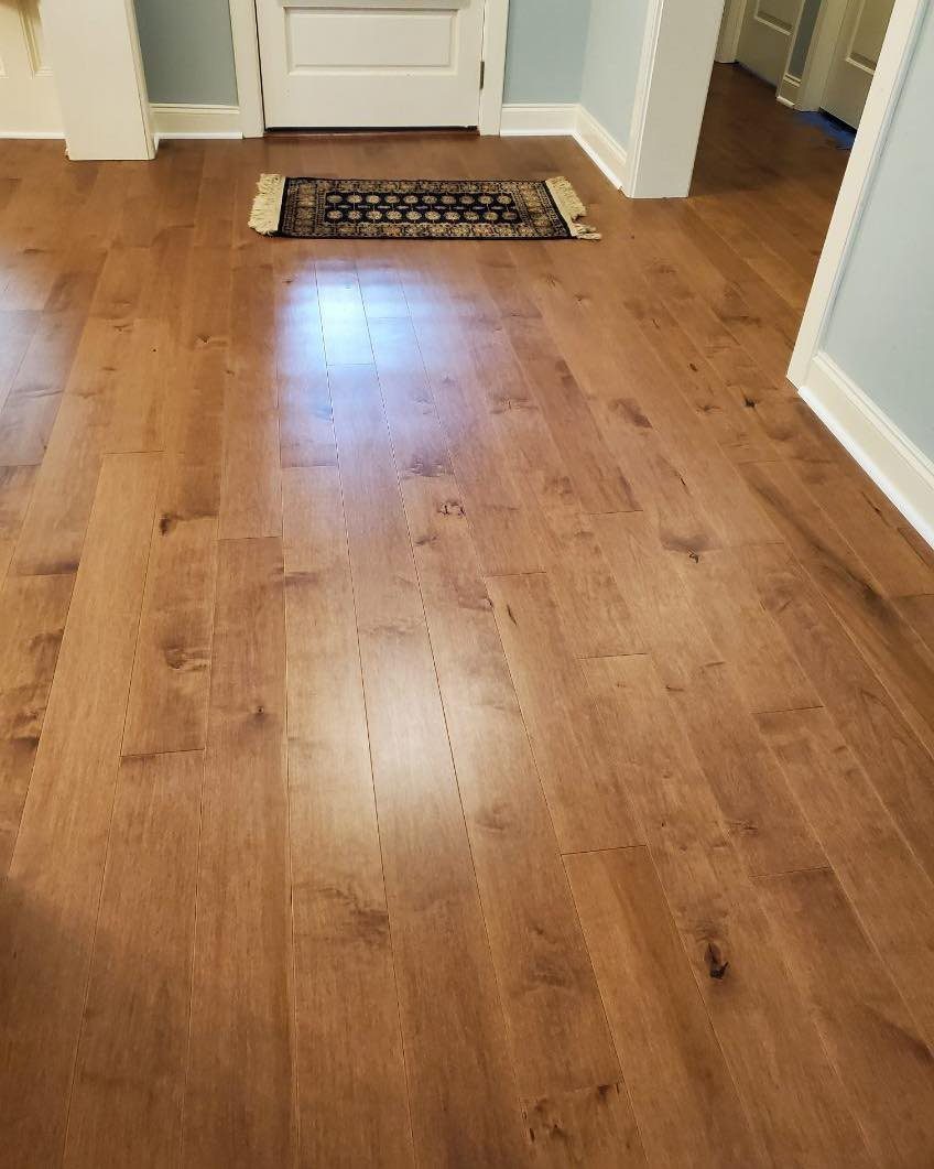 Medium Hardwood Floors: 5 Rooms That Get the Tone Right 4 Polished medium-toned hardwood floor planks reflecting light in a home hallway near a white door.