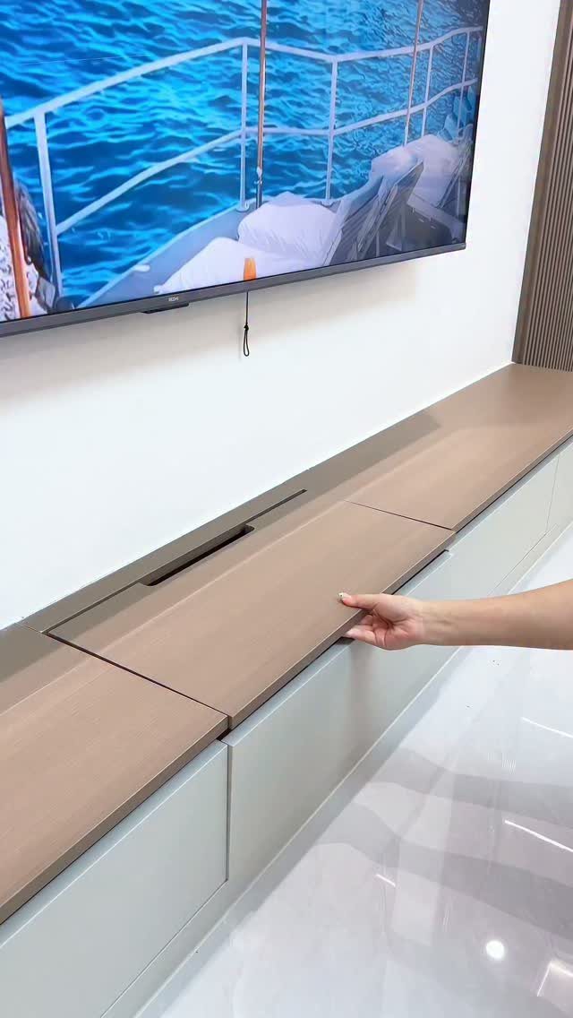 A hand opening a hidden compartment in a long, light wood media console.