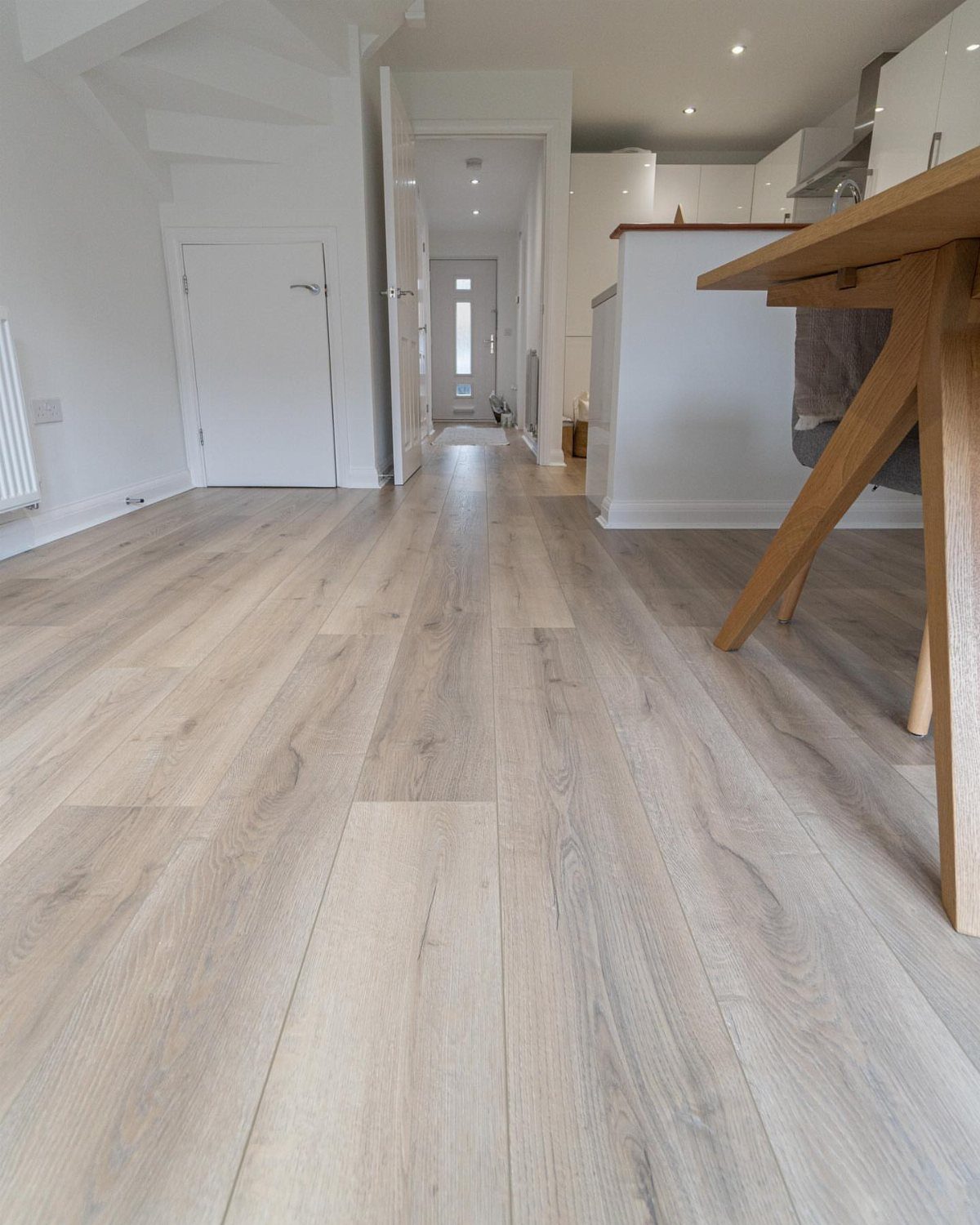 10 Modern Farmhouse Flooring Ideas for Every Room 3 Light wood-look laminate flooring stretching through a bright modern home hallway and kitchen.