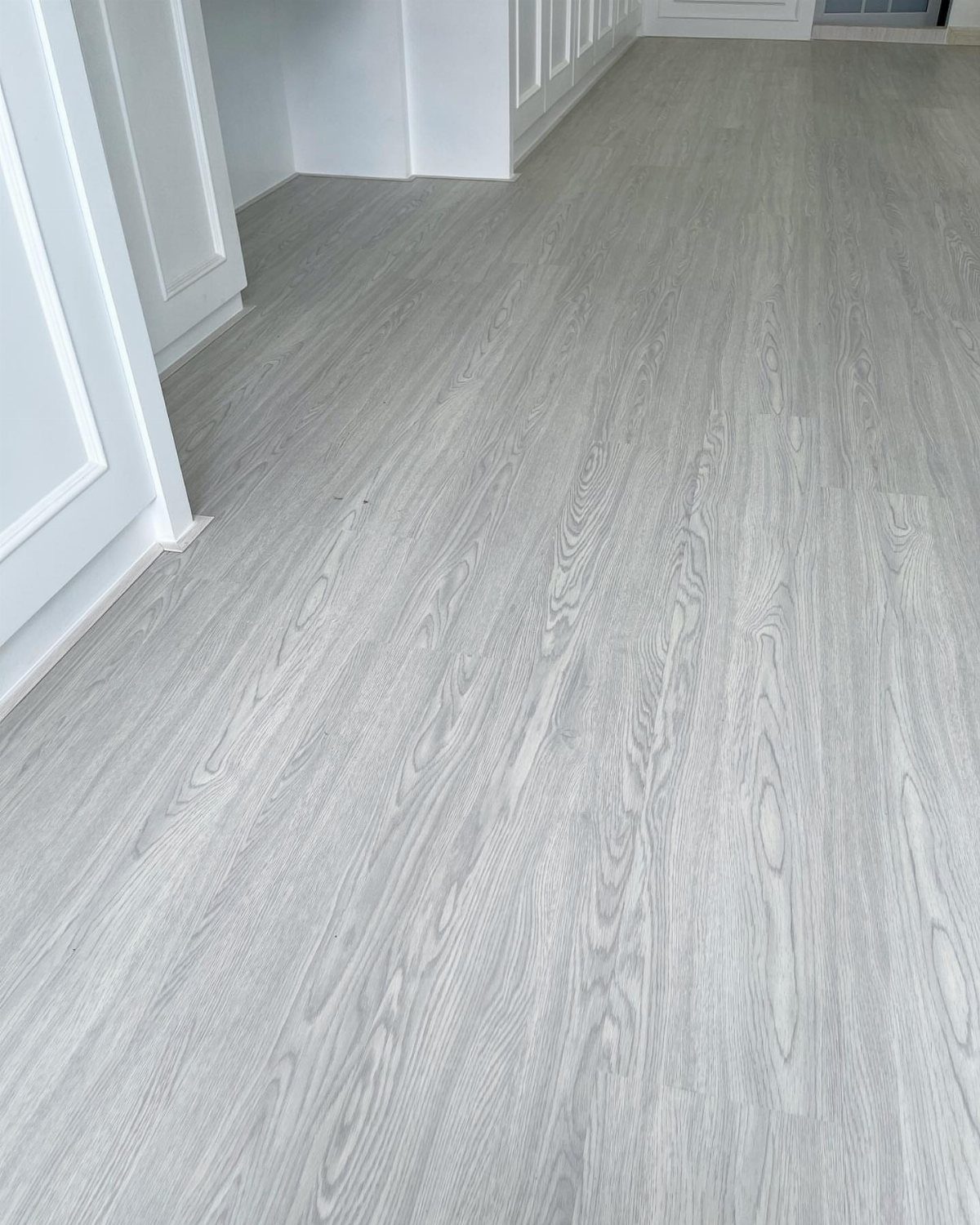 10 Modern Farmhouse Flooring Ideas for Every Room 6 Light grey wood-look planks installed on the floor of a bright room with white walls.