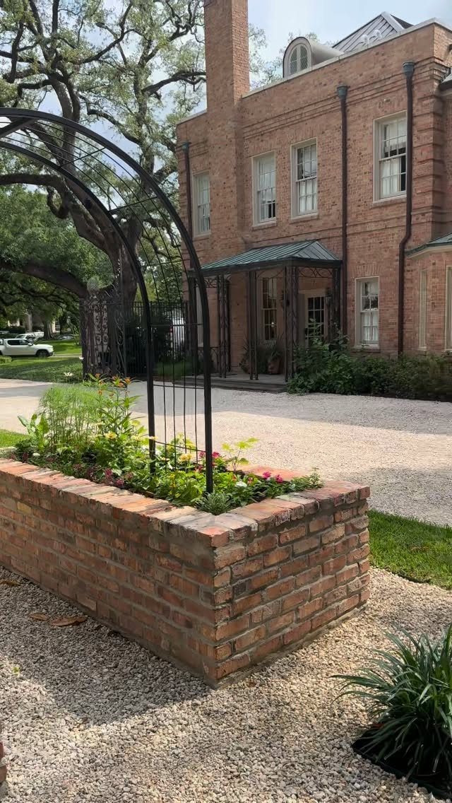 Painted Raised Garden Beds: 11 Ideas for Your Yard 7 Red brick raised garden bed with a black metal arch trellis and green plants.