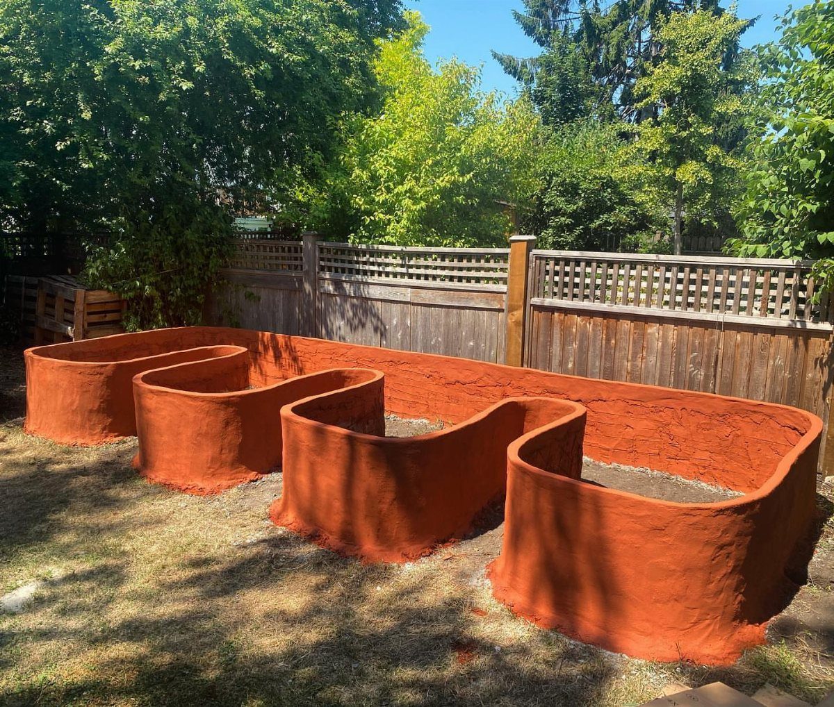 Painted Raised Garden Beds: 11 Ideas for Your Yard 9 Terracotta-orange winding raised garden bed in a sunny backyard with a wooden fence.