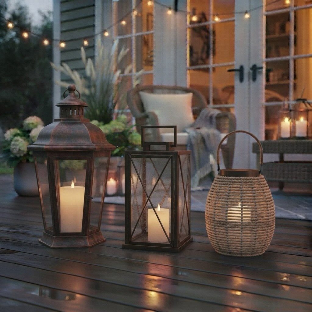 25 Patio Lights Ideas, From String Lights to Step Lighting 9 Three lit candles in different lanterns on a dark wooden outdoor patio deck.