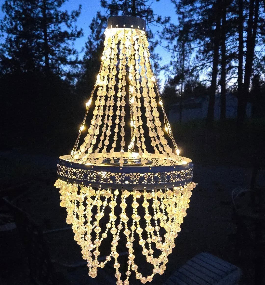 25 Patio Lights Ideas, From String Lights to Step Lighting 16 Outdoor crystal chandelier with glowing lights hanging against a twilight forest backdrop.
