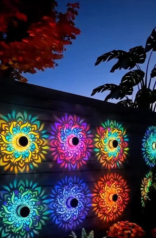 25 Patio Lights Ideas, From String Lights to Step Lighting 20 Colorful mandala light projections illuminating a dark wooden fence in a garden setting.