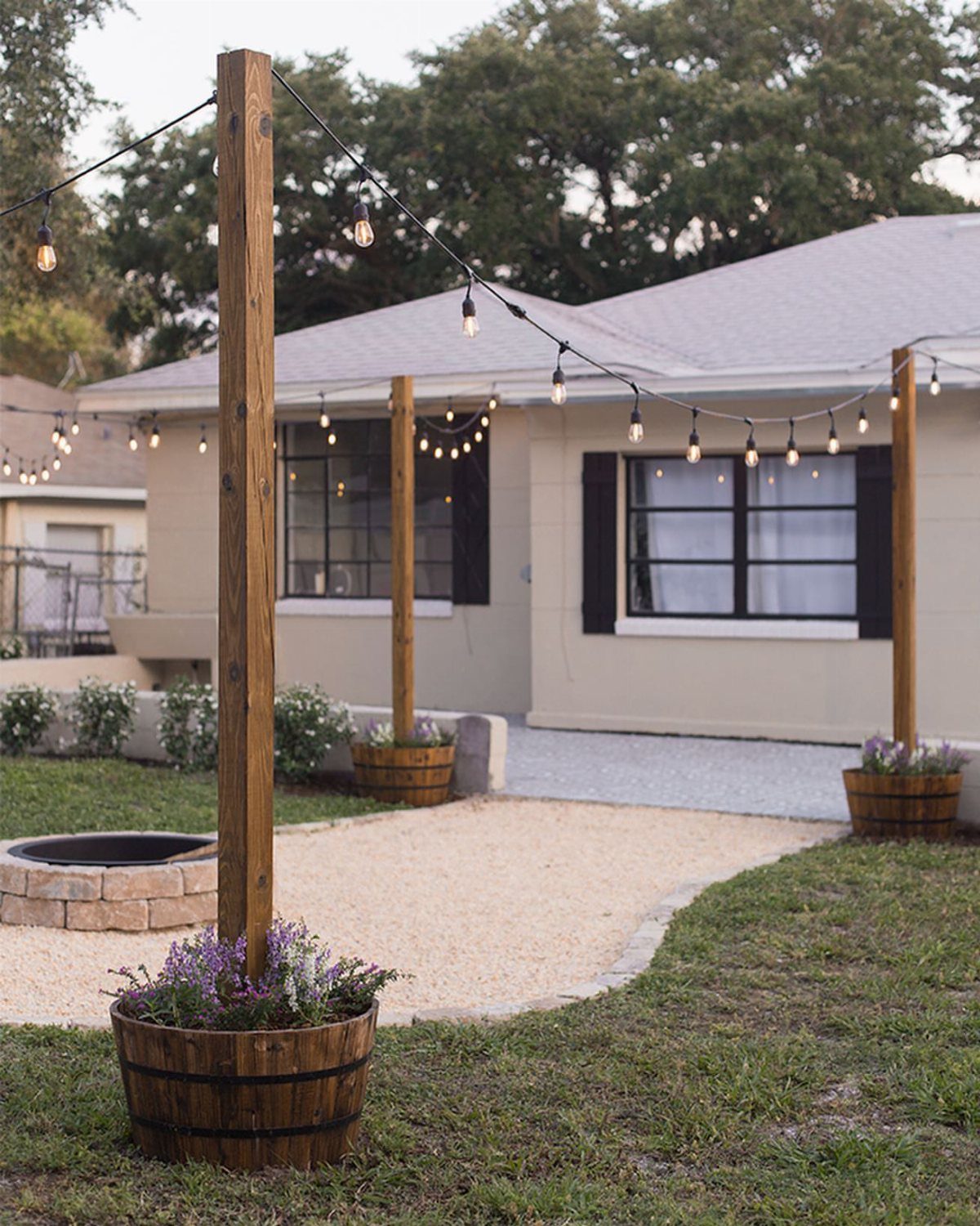 25 Patio Lights Ideas, From String Lights to Step Lighting 12 String globe lights draped between wooden posts in barrels on a residential patio.