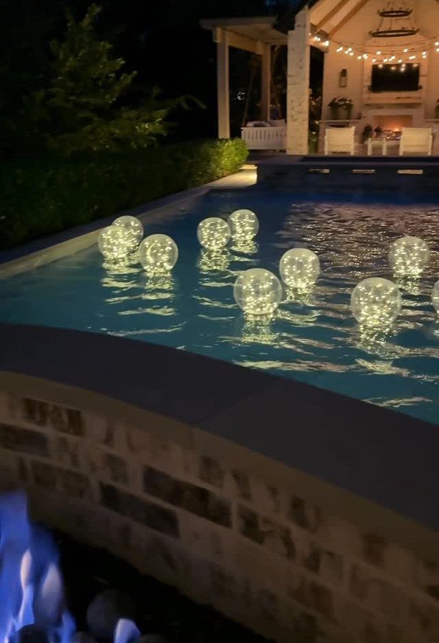 25 Patio Lights Ideas, From String Lights to Step Lighting 6 Glowing white spherical lights floating on a swimming pool at night.