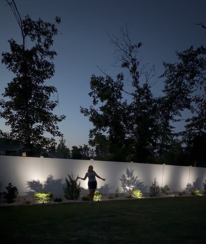 25 Patio Lights Ideas, From String Lights to Step Lighting 17 Spotlights in a garden casting beams of light against a white backyard fence