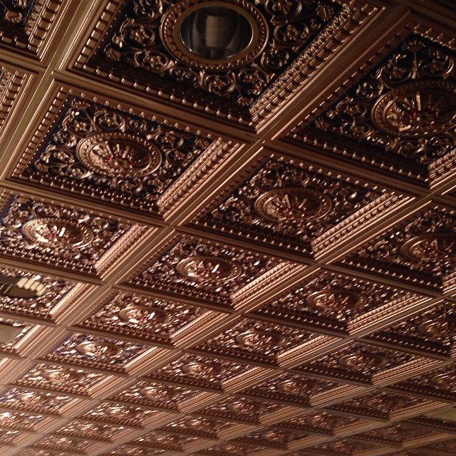 Ornate metallic bronze ceiling tiles with intricate embossed patterns and circular central motifs.