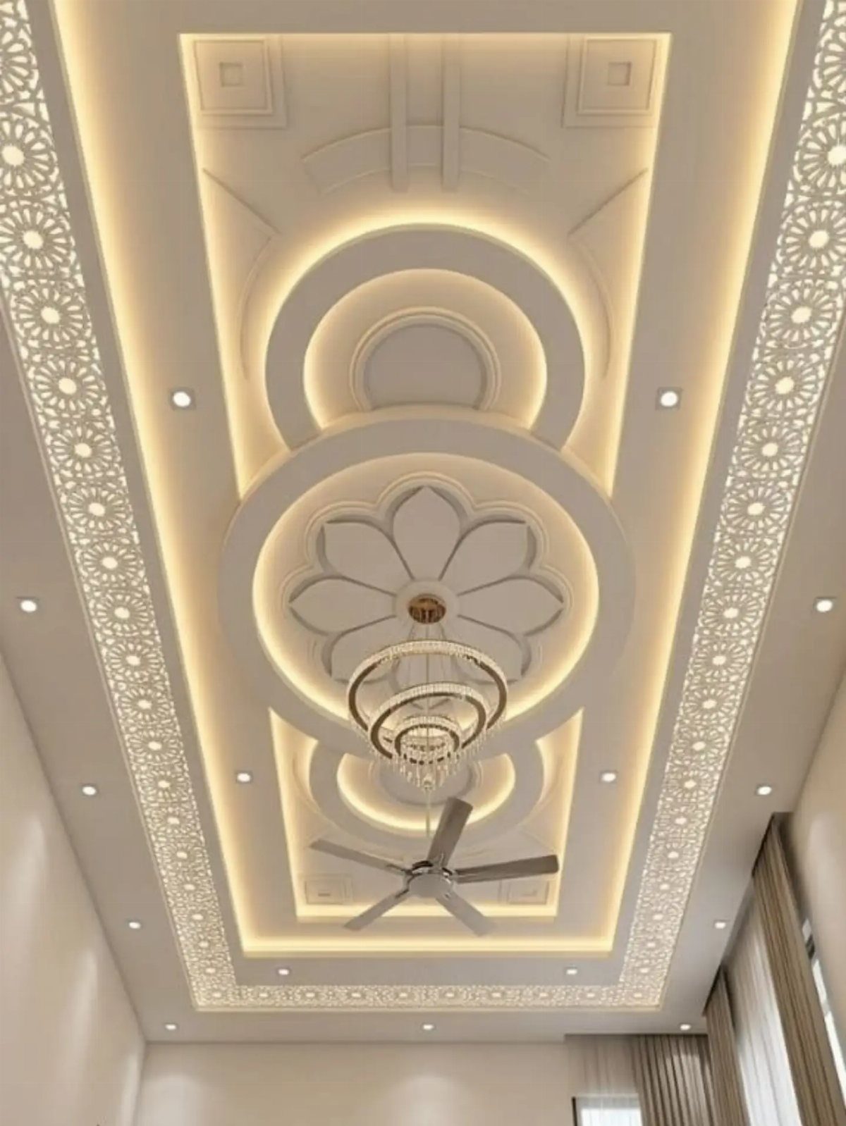 A layered white false ceiling with circular patterns and warm LED cove lighting.