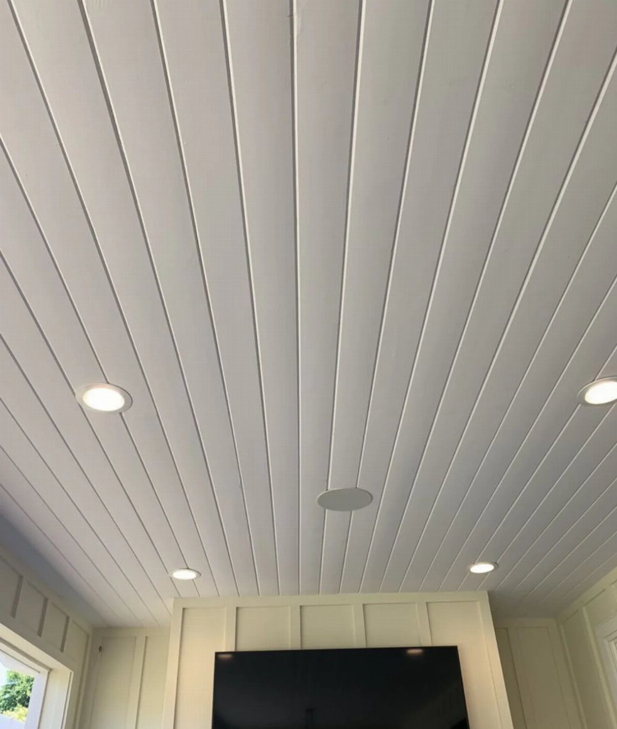 White paneled ceiling with long vertical slats and recessed circular lights in a room.