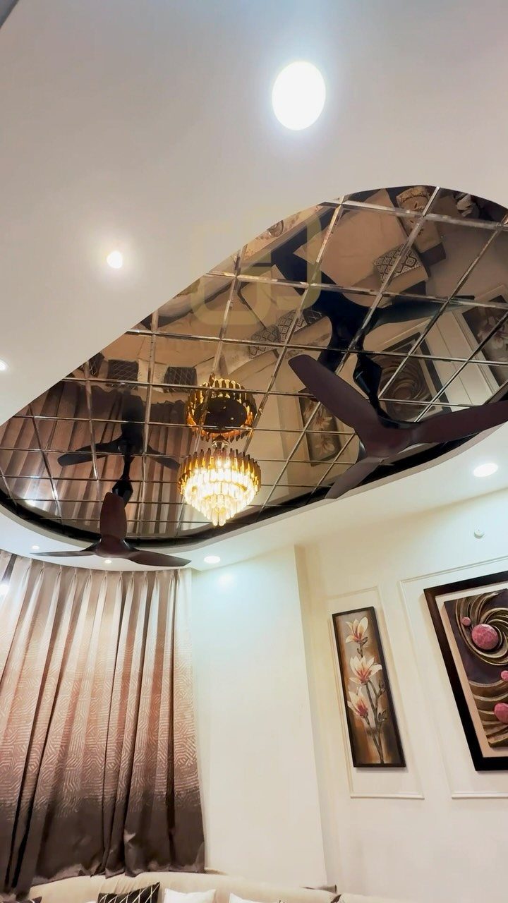 Modern room ceiling with an oval mirrored pop design, crystal chandelier, and fan.