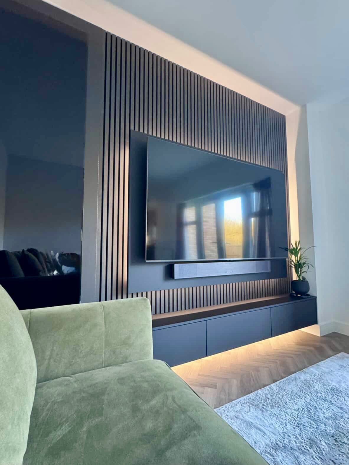A television mounted on a dark vertical wood slat wall above a floating console.