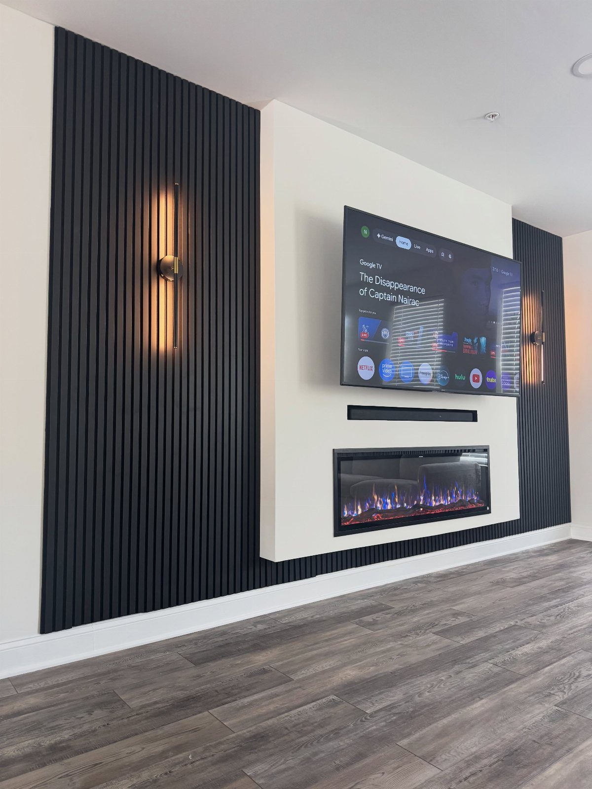 Black slat wall panels flanking a white wall section with a mounted television and electric fireplace.