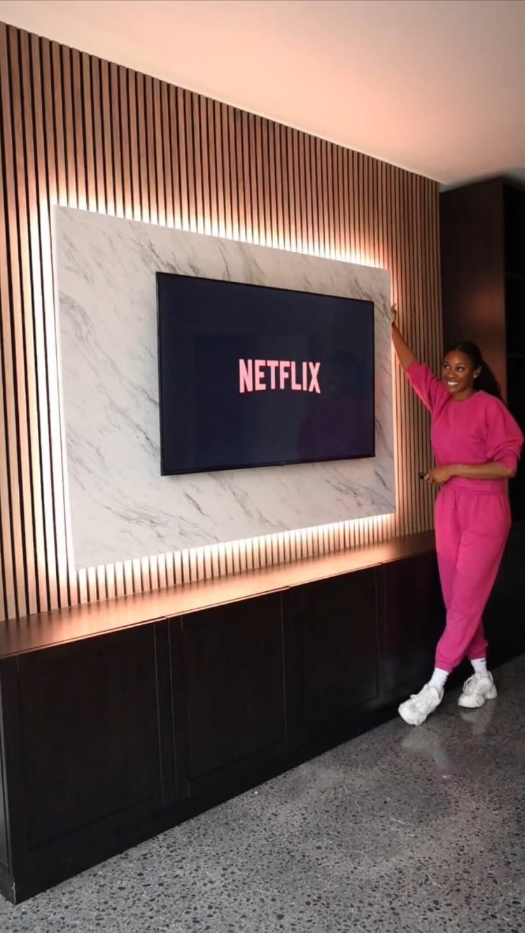 Television mounted on a marble panel set against a backlit wooden slat wall.