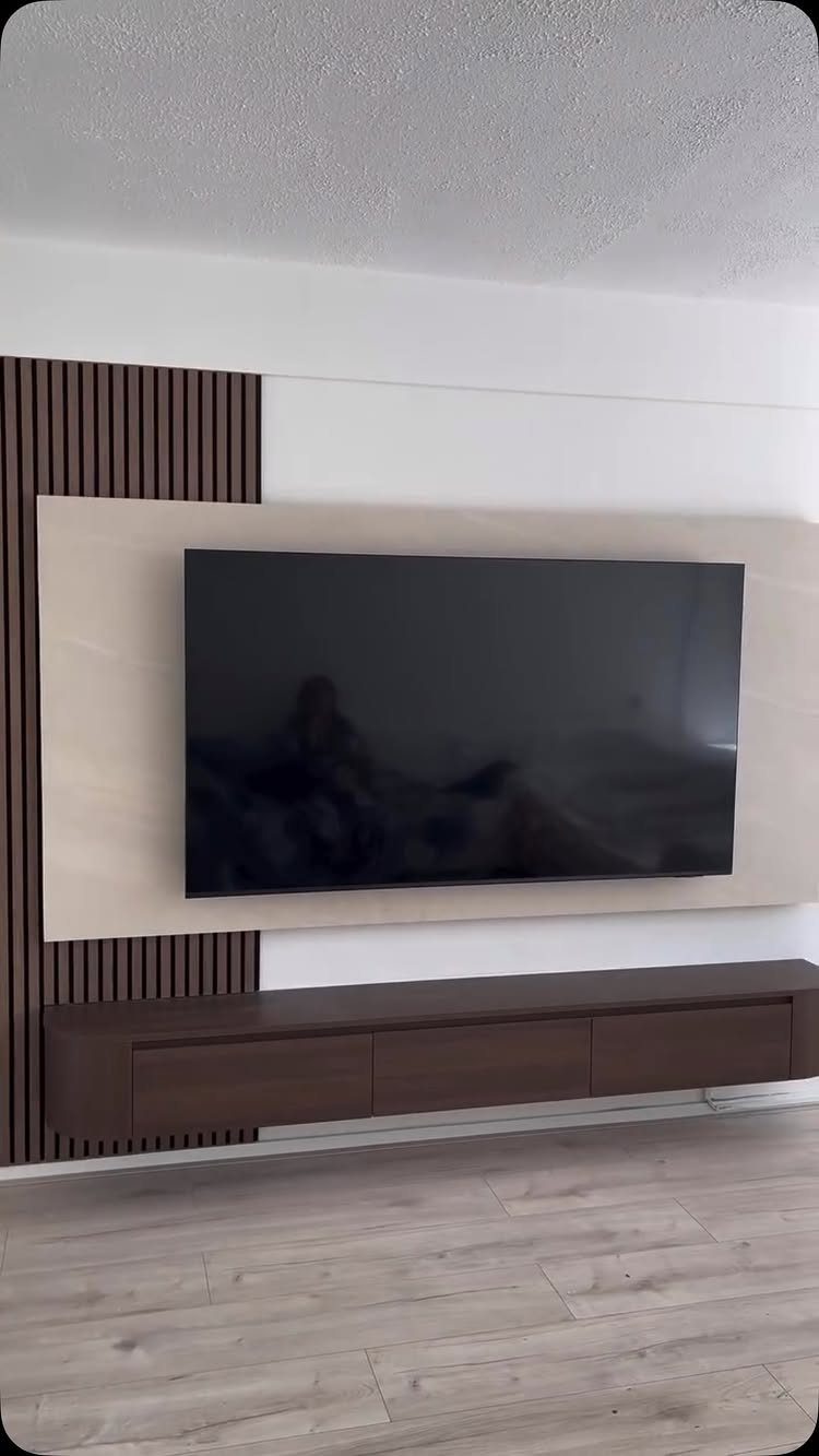 Television mounted on a light wood panel with dark brown slat wall accents on the left.