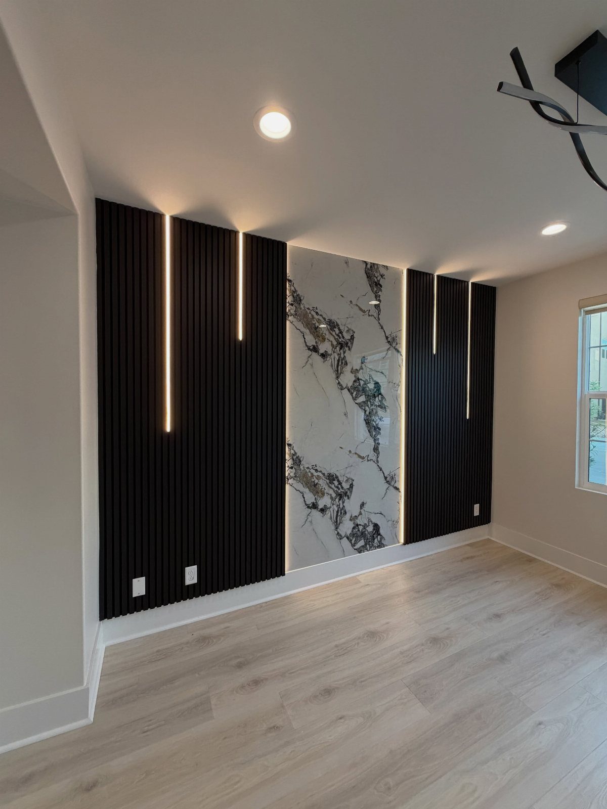 Black slat wall panels with integrated vertical strip lighting flanking a marble wall feature.