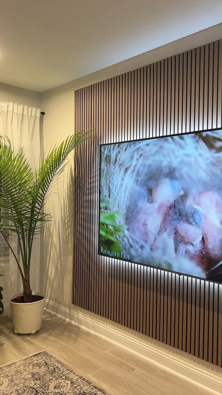 A television mounted on a vertical wood slat wall next to a potted palm plant.