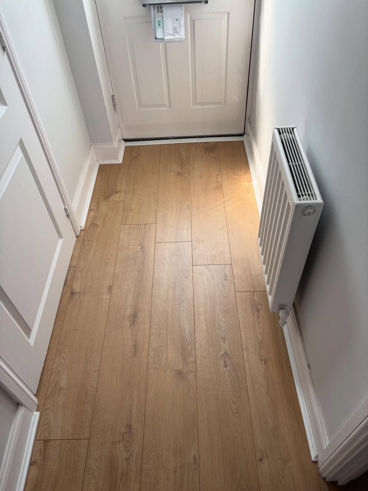 Types of Flooring: 10 Ideas from Hardwood to Rubber 1 Light brown wood-effect laminate flooring planks in a narrow white hallway.