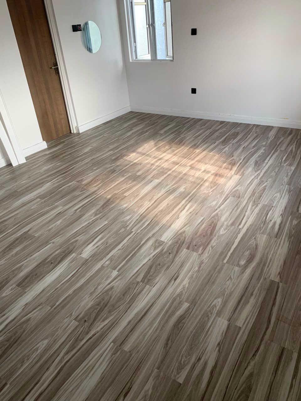 Types of Flooring: 10 Ideas from Hardwood to Rubber 2 Wood-grain patterned vinyl flooring in a bright room with white walls and a wooden door.