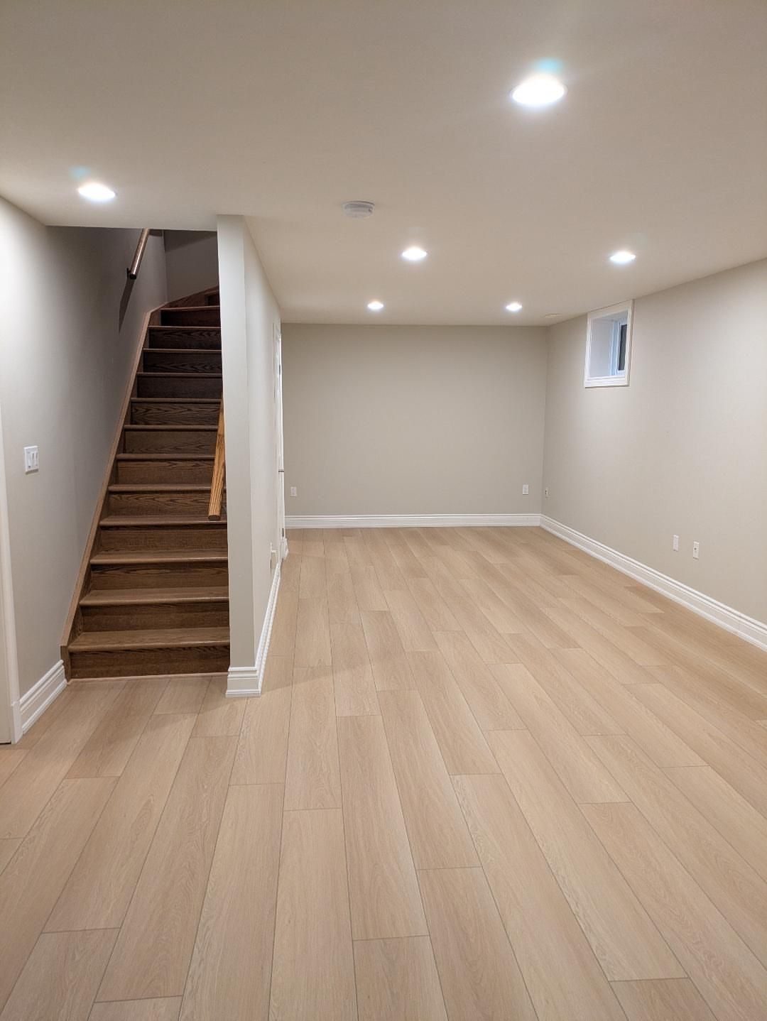 9 Vinyl Floor Colors for Every Room in 2026 1 Light sandy taupe vinyl plank flooring in an empty room with a wooden staircase.