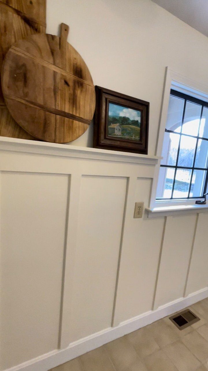 White board-and-batten wainscoting paneling on a wall below a decorative ledge and window.