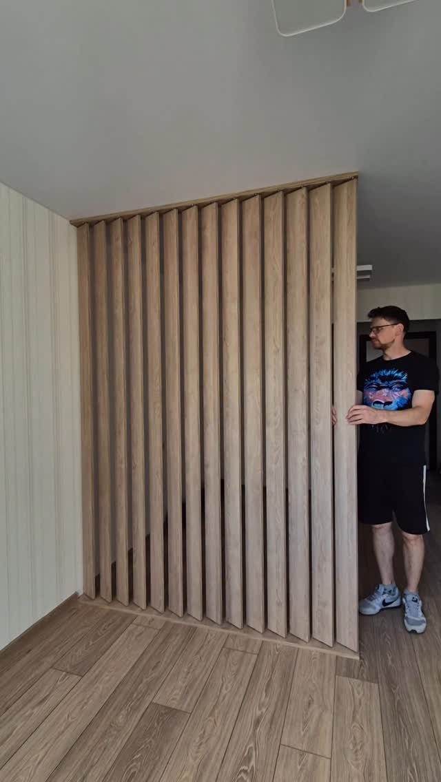 Vertical wooden slat partition wall dividing a room with a man standing beside it.
