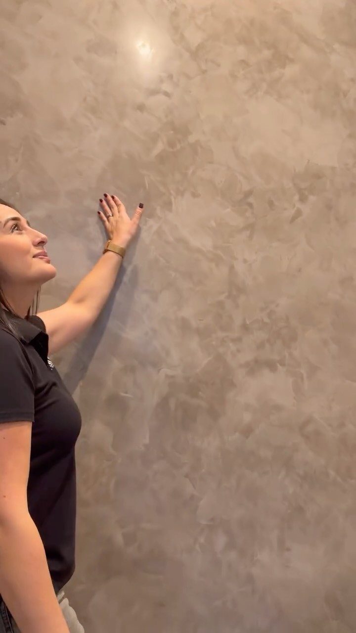 Wall Texture Design: 12 Ideas for Every Room 9 A woman touching a smooth, polished grey Venetian plaster wall with marble-like textures.