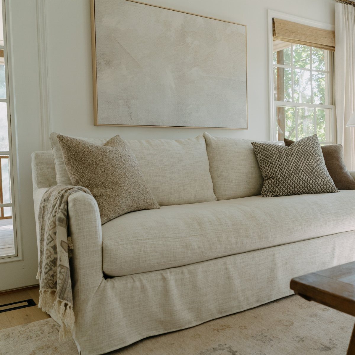 White slipcovered sofa with neutral pillows and abstract art in a bright room.