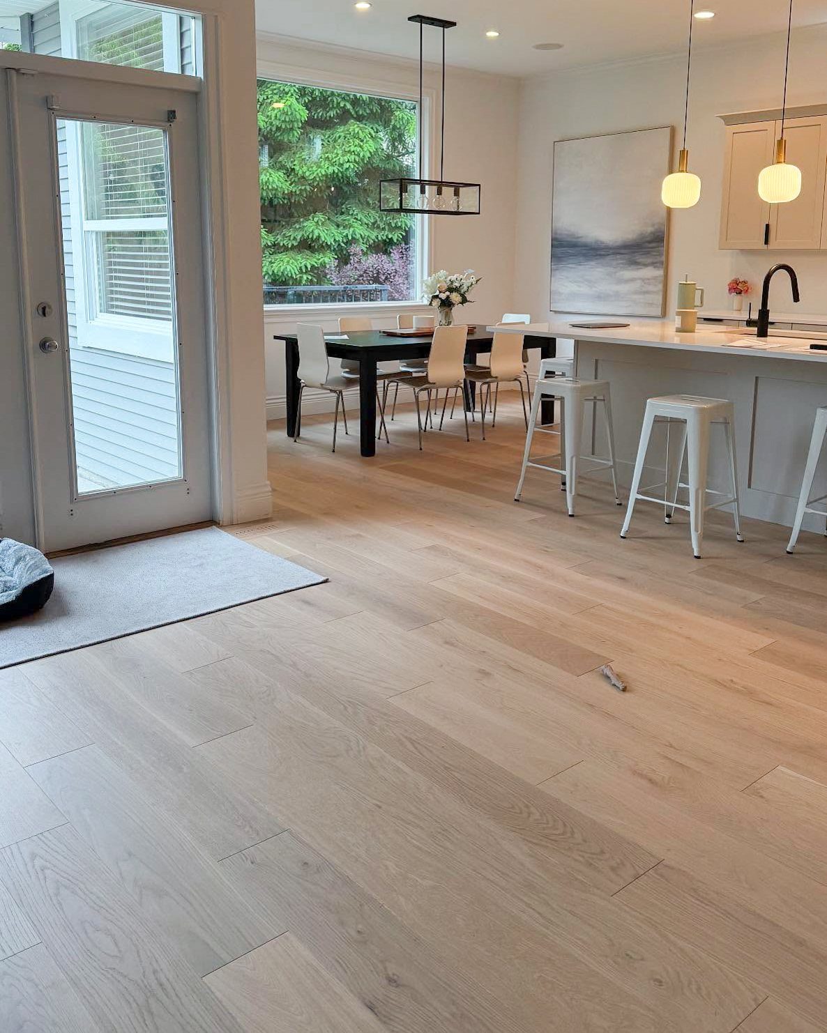Light-colored wide-plank wooden floors in a bright white kitchen and dining area.