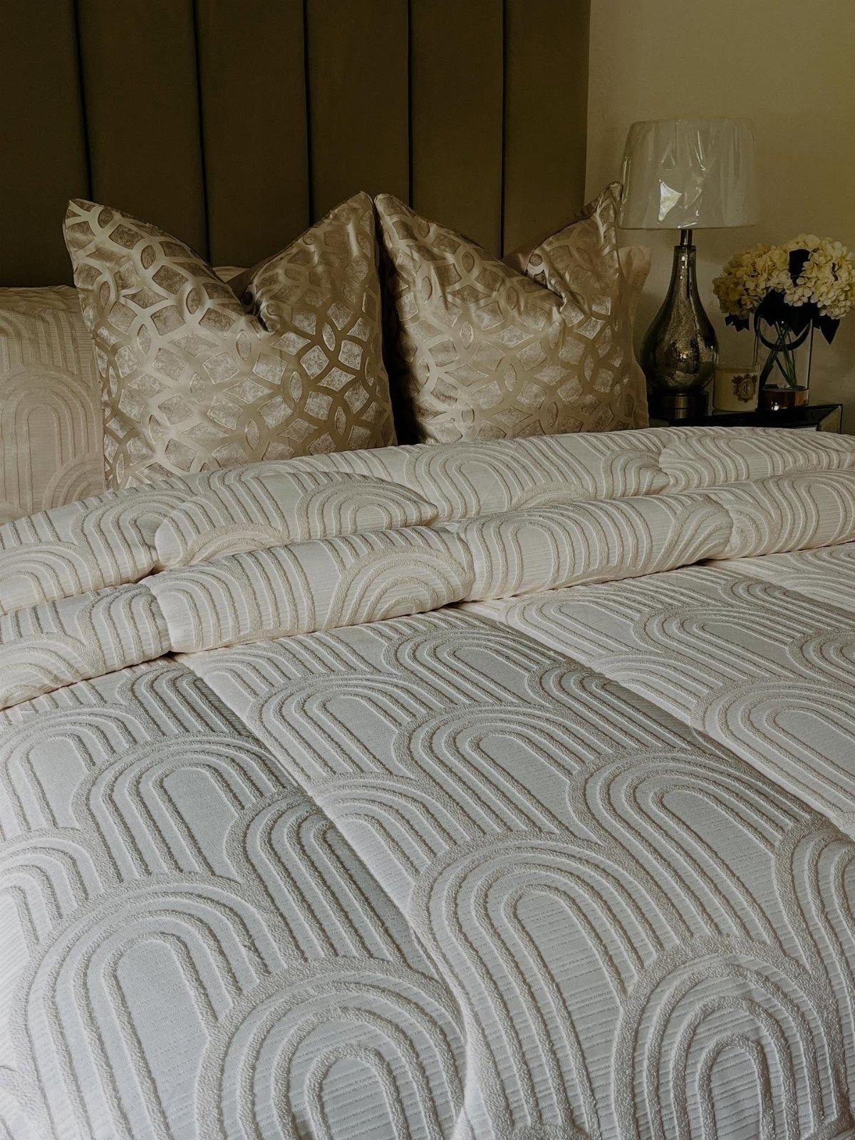 Gold-toned decorative pillows on a bed with textured white bedding and brown headboard.