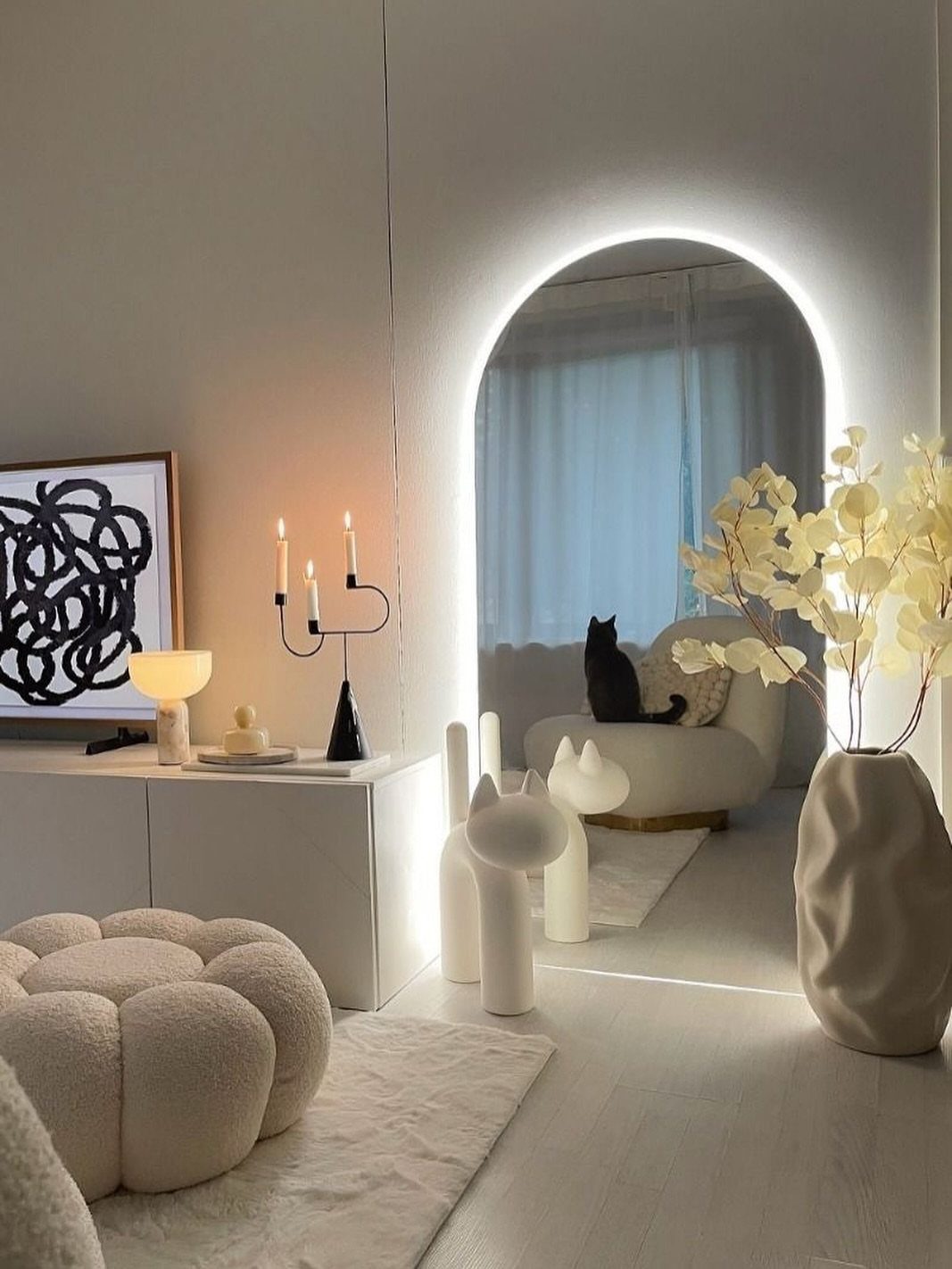 Arched backlit mirror in a minimalist white room with modern furniture and decor.