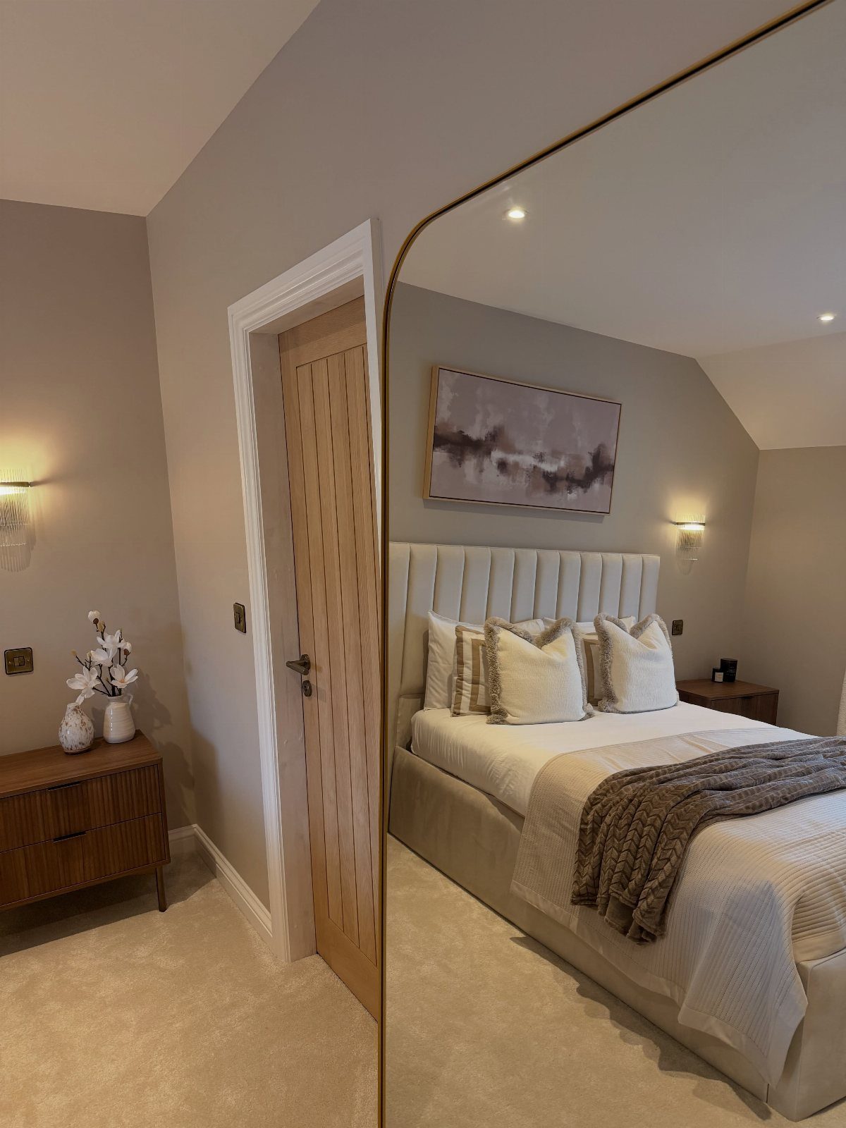 White bed with a brown throw blanket reflected in a gold-framed mirror.