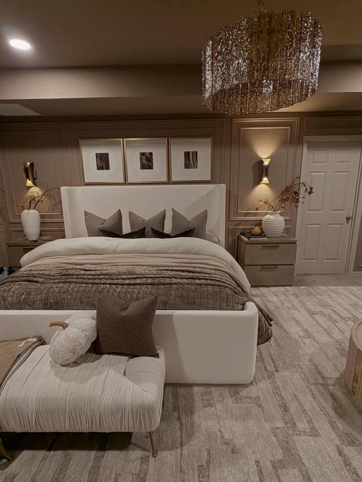 White bed with neutral bedding and a crystal chandelier in a taupe bedroom.