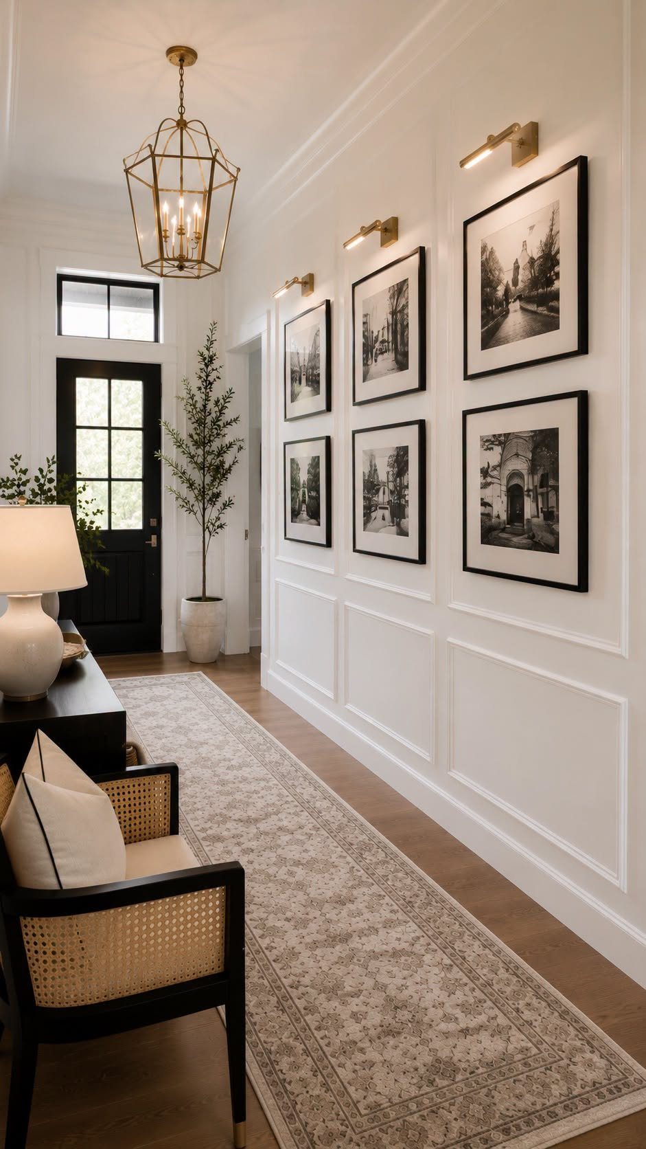 White entryway hallway with black-framed art on paneled walls and a patterned runner.