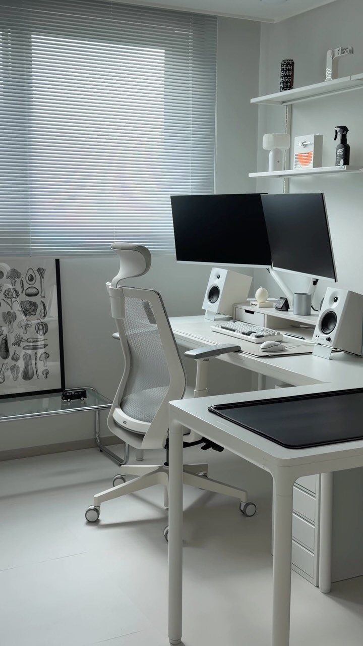 White home office with a white desk, ergonomic chair, and dual black monitors.